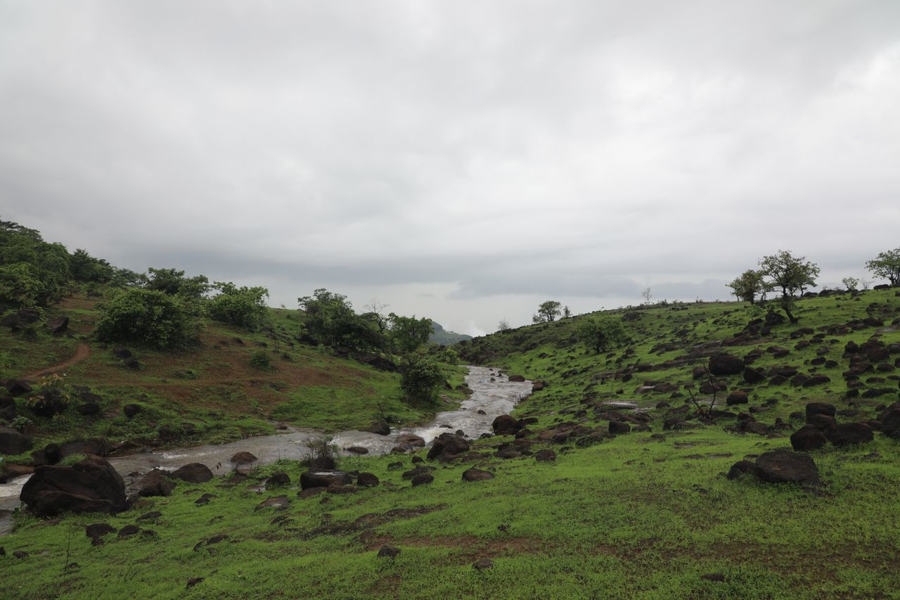 A scenic view of rolling green hills with a stream flowing through under a cloudy sky.