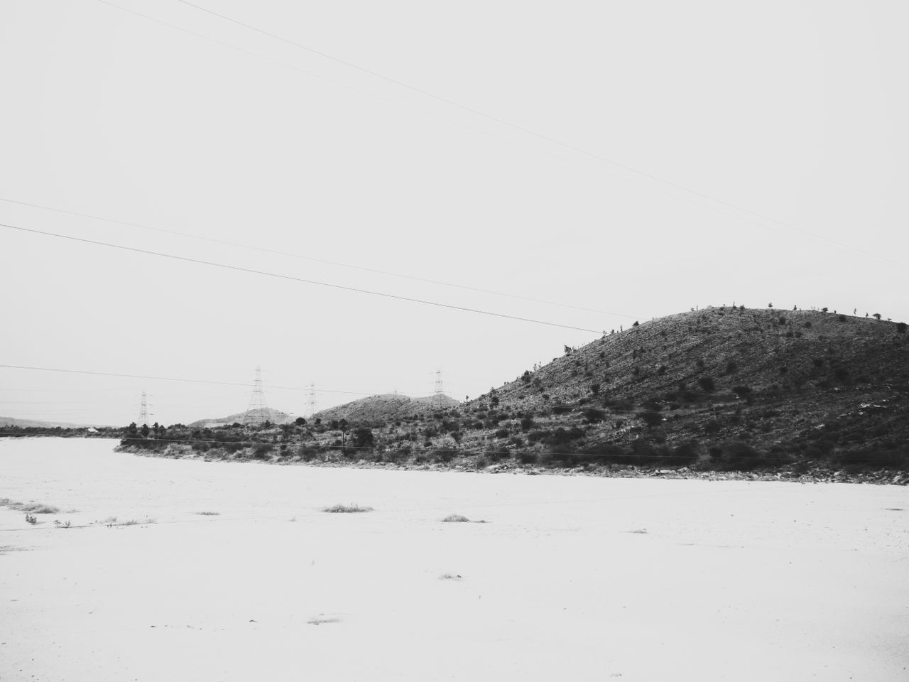 A monochromatic view of barren hills with transmission towers under an overcast sky, evoking a sense of solitude.